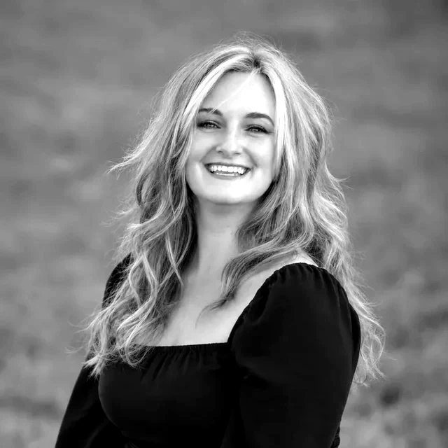 Portrait of Andrea Salad, smiling, with long wavy blonde hair, outdoors.